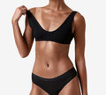A woman in matching black ribbed bra and underwear poses against a plain white background, highlighting her flawless glow from BondiSandsEU Ultra Dark Salon Solution.