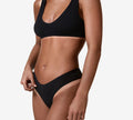 A woman in a black ribbed sports bra and matching underwear stands against a white background, highlighting her flawless tan—ideal for fans of the BondiSandsEU Salon Solution Ultra Dark. Her head and legs are not visible.