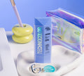 A blue bottle of BondiSandsEU Sapphire Technocolor Self Tanning Face Serum sits on a textured white tray with a silver keyring and teal ring, with a pastel yellow apple pen holder and iridescent zipper pouch in the background.