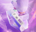 A bottle of BondiSandsEU Magenta Technocolor 1 Hour Express Self Tanning Foam sits on a clear acrylic block next to a purple tanning mitt, set against a shiny purple background with the mitt’s reflection visible below.