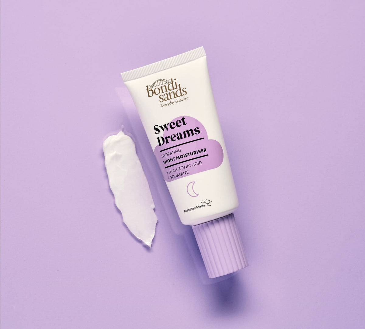 A tube of BondiSandsEU Sweet Dreams Night Moisturiser rests on a lavender background beside a swipe of white cream, emphasizing intense hydration with hyaluronic acid and squalane.