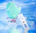 A turquoise tanning mitt and a bottle of BondiSandsEU Sapphire Technocolor 1 Hour Express Self Tanning Foam sit on a clear acrylic tray, reflected against a blue watery background for an effortless, natural glow.