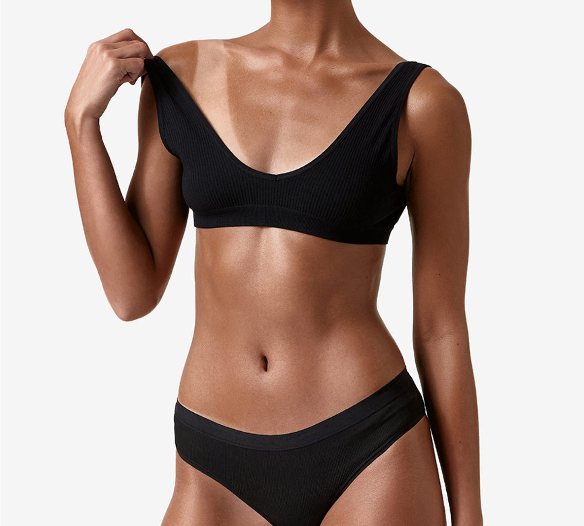 A woman in a black bra and panties set stands against a white background, holding one bra strap away to showcase her flawless glow from the BondiSandsEU Dark Salon Solution 1L Duo fast-drying spray tan.
