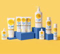 Nine BondiSandsEU sunscreen products with yellow and blue labels are displayed on blue blocks against a yellow background, including everyday bottles, tubes, and the Face SPF 50+ Tinted Everyday Sunscreen Fluid.