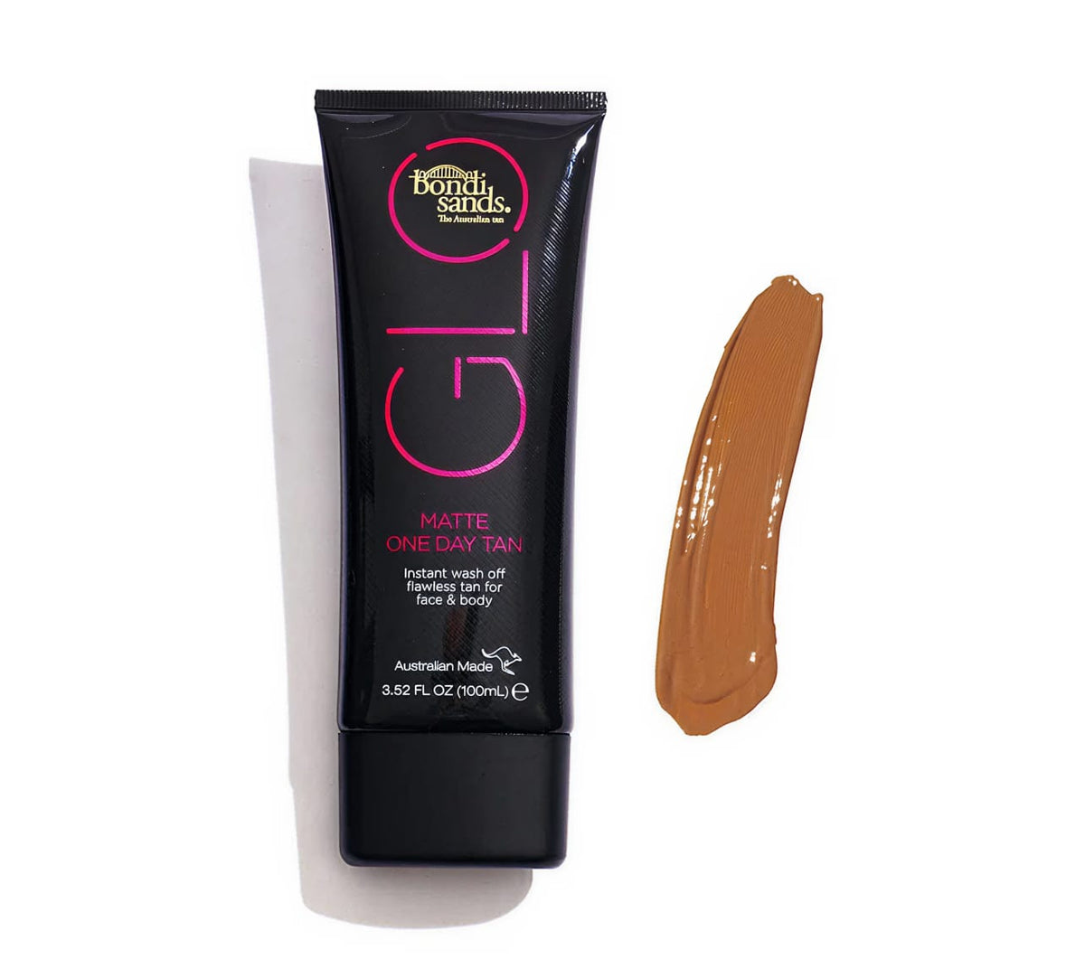 A black tube of BondiSandsEU GLO Matte One Day Tan lies next to a streak of tan cream, highlighting its natural matte shade. The tube displays pink and gold branding, with the cap placed at the bottom.
