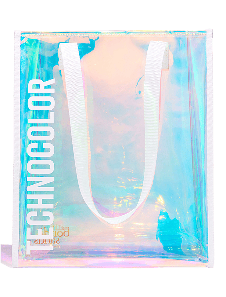 The BondiSandsEU Technocolor Tote Bag features iridescent holographic material, white handles, and TECHNICOLOR printed vertically in bold white letters—a stylish limited edition accessory for any outing.