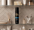 A bathroom shelf displays the BondiSandsEU Dark Self Tanning Foam & Application Mitt Bundle, surrounded by skincare products and brushes, set against a herringbone-patterned tiled wall.