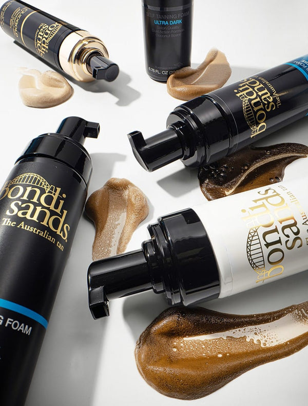 Four bottles of BondiSandsEU Self Tanning Foam 1 Hour Express sit on a white surface, each with the foam dispensed beside them in varying shades from light to dark.