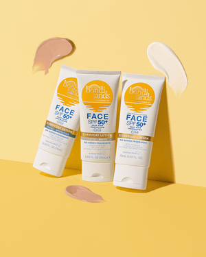 Three BondiSandsEU SPF 50+ Everyday Face Sunscreen Lotion tubes stand upright on a yellow surface, surrounded by beige and white lotion smears. Each tube has yellow and blue labels with white caps.