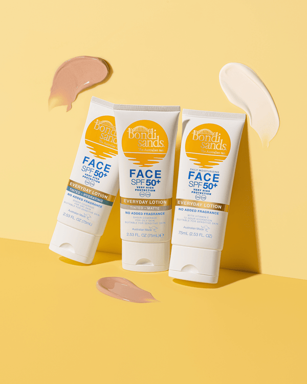 Three BondiSandsEU SPF 50+ Everyday Face Sunscreen Lotion tubes stand upright on a yellow surface, surrounded by beige and white lotion smears. Each tube has yellow and blue labels with white caps.