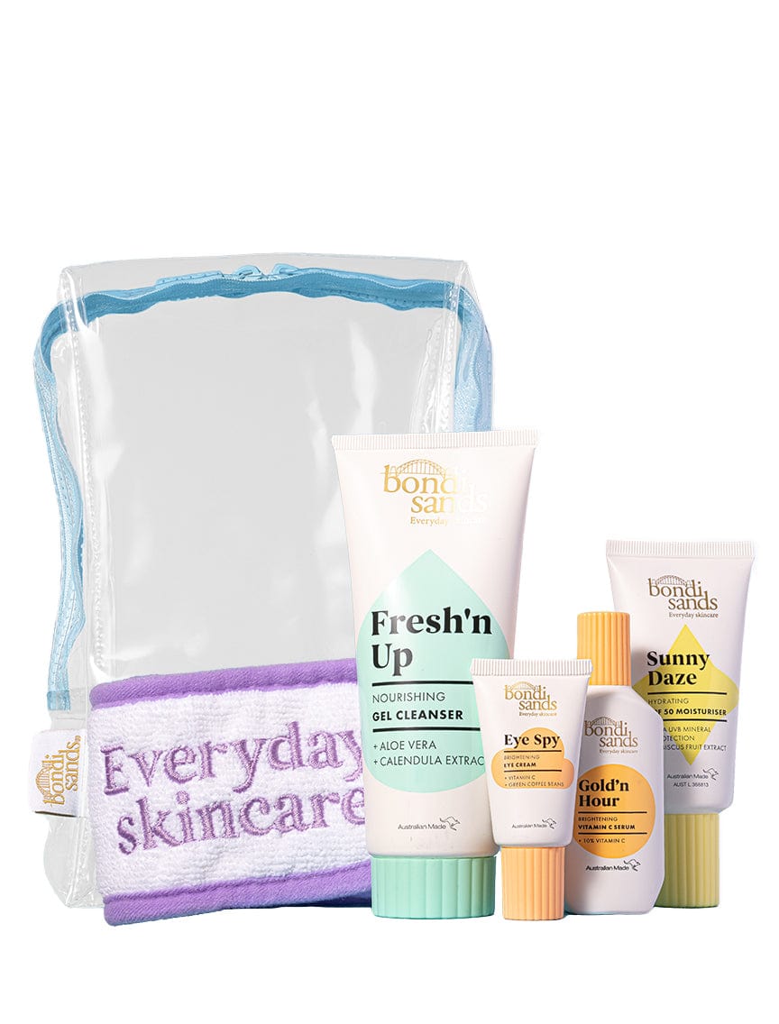 The BondiSandsEU Brightening Besties Gift Set features five skincare essentials in white packaging with pastel accents, all packed in a clear toiletries bag with blue trim—includes a purple headband, gel cleanser, eye cream, SPF 50 moisturiser, and sunscreen.