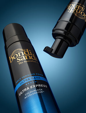 A Bondi Sands Europe Ultra Express Self Tanning Foam bottle with ColourLock Accelerator stands upright, while another bottle with the pump facing forward is displayed above against a blue gradient background.