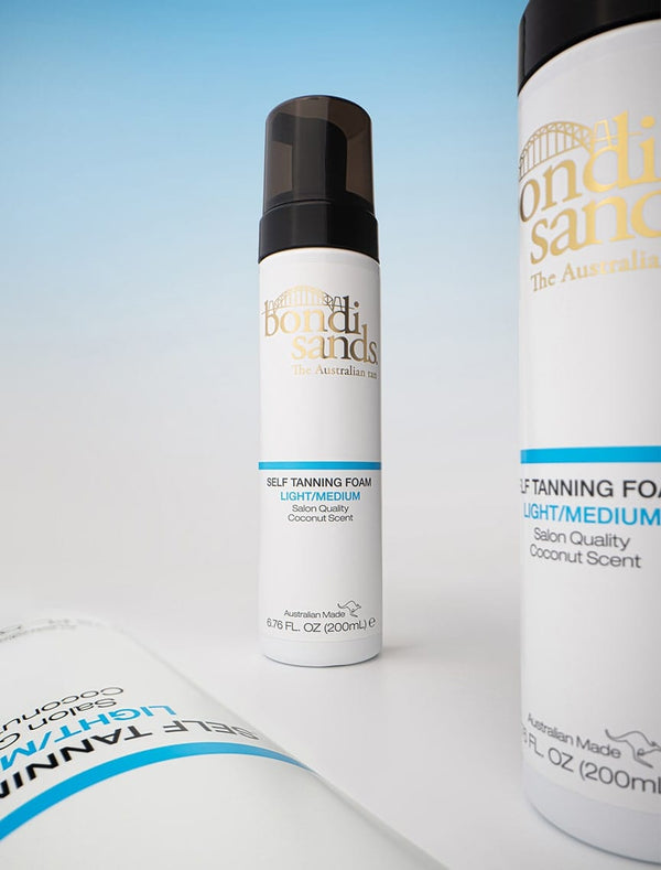 A bottle of BondiSandsEU Self Tanning Foam Light Medium, 200mL, stands upright with two partially visible bottles nearby against a graduated light blue background—ideal for achieving a signature Australian tan.