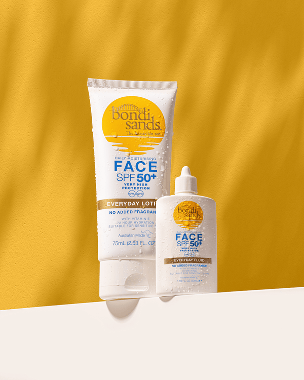 The BondiSandsEU SPF 50+ Everyday Face Fluid in a tube and a bottle stand upright on a yellow and white background, both labeled with UVA and UVB protection, with water droplets accentuating their freshness.