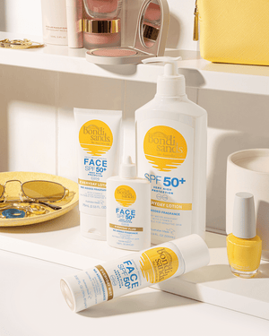 A BondiSandsEU SPF 50+ Everyday Sunscreen Lotion Pump sits on a yellow-themed bathroom counter, surrounded by sunglasses, a ring, nail polish, and a yellow purse for a sunny, stylish setup.
