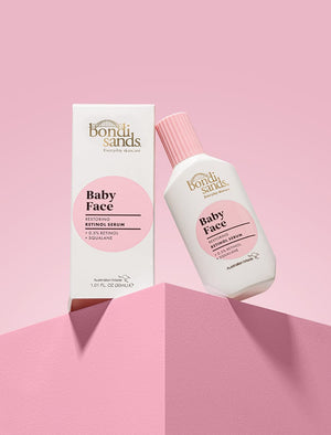 A white bottle and box of BondiSandsEU Baby Face Retinol Serum, with pink labels, are displayed on a pink geometric surface against a gradient pink background—ideal for reducing fine lines and supporting youthful-looking skin.