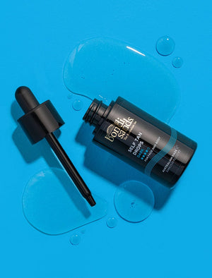 A black BondiSandsEU Self Tan Drops Dark bottle rests on a bright blue surface with the cap and dropper off; clear drops surround it, evoking the essence of an Australian tan.