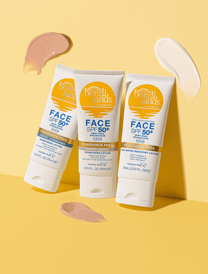 Three BondiSandsEU SPF 50+ Fragrance Free Hydrating Tinted Face Lotion tubes are arranged on a yellow background, with swatches of beige, pink, and cream tinted lotion surrounding them.