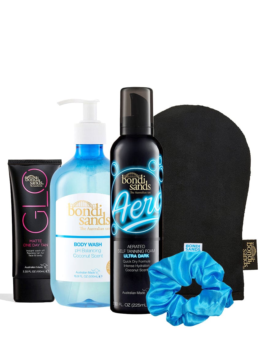The Bondi Sands X Carli Bybel Bundle by BondiSandsEU includes self tanning foam, a matte one day tan tube, coconut body wash with pump, a black tanning mitt, and a blue scrunchie arranged together.
