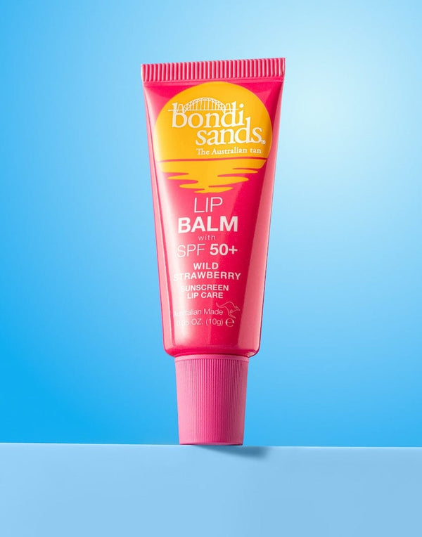 A pink tube of BondiSandsEU SPF 50+ Lip Balm Wild Strawberry with nourishing shea butter stands upright on a light blue background, featuring yellow and white text plus a sun graphic on the label.