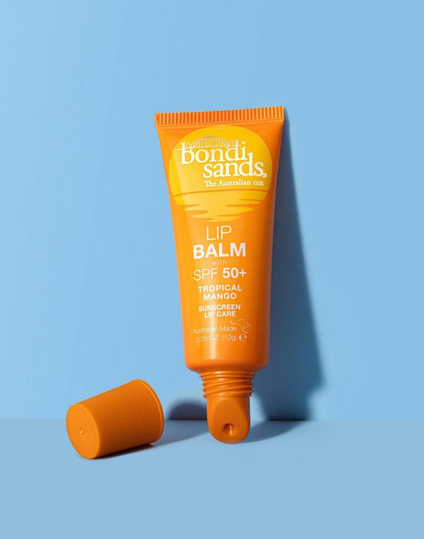 A BondiSandsEU SPF 50+ Lip Balm Tropical Mango with nourishing Shea Butter stands upright on a blue surface, its orange tube uncapped and the cap lying beside it.