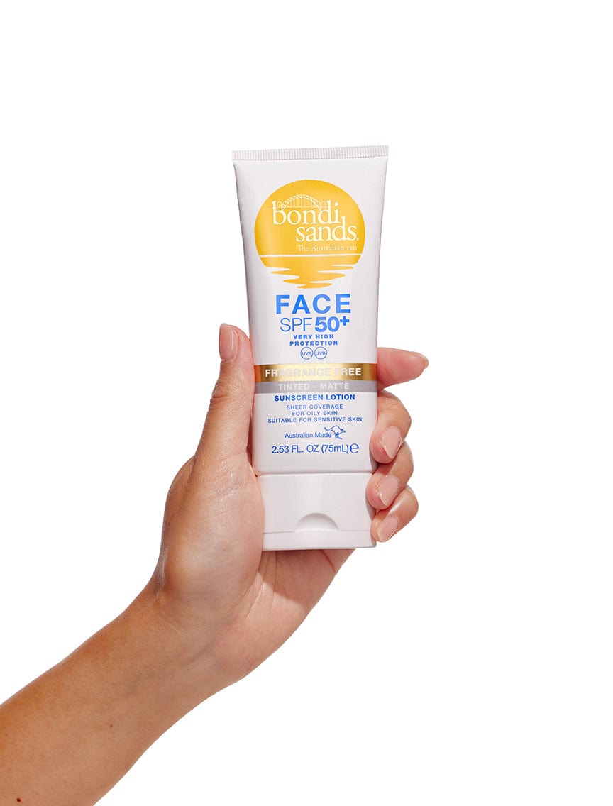 A hand holds a tube of BondiSandsEU Face SPF 50+ Tinted & Matte Sunscreen Lotion (2.53 fl oz/75 mL) with yellow and blue accents, designed for oily skin to protect and mattify without excess shine against a white background.