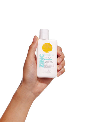 A hand holds a white bottle of BondiSandsEU SPF 50+ Mineral Face Fluid, featuring a yellow and blue design, offering invisible sun protection against a plain white background.
