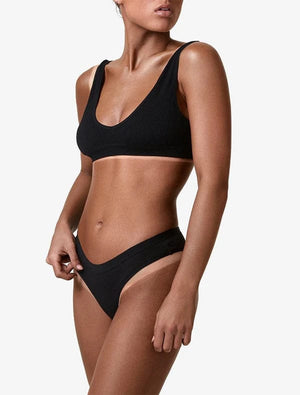 A woman with a flawless BondiSandsEU Salon Solution Ultra Dark professional spray tan poses in a black bikini with a scooped neckline and high-cut bottoms, showing her upper body against a plain white background.