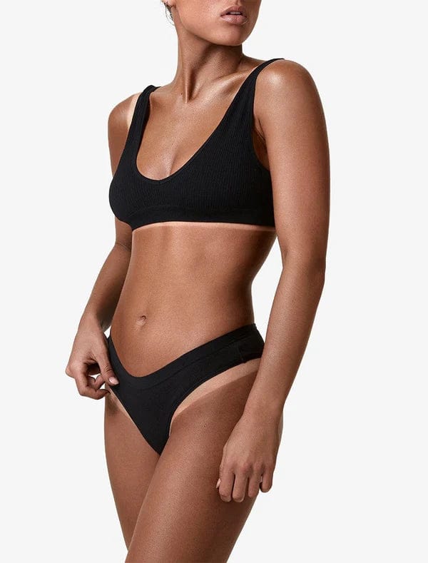 A woman with a flawless BondiSandsEU Salon Solution Ultra Dark professional spray tan poses in a black bikini with a scooped neckline and high-cut bottoms, showing her upper body against a plain white background.