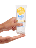 A hand squeezes BondiSandsEU Face SPF 50+ Tinted & Matte Sunscreen Lotion from a white and yellow tube onto fingers, demonstrating product application.