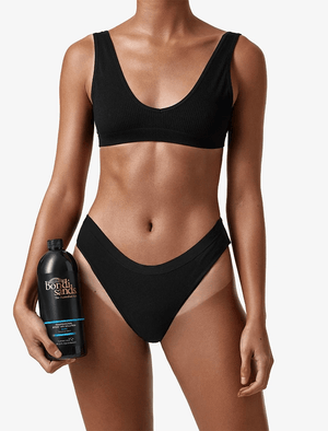 A woman in a black bikini holds a black bottle of BondiSandsEU Salon Solution Dark Duo against a white background. Her skin looks evenly tanned and flawless, showcasing a streak-free finish.